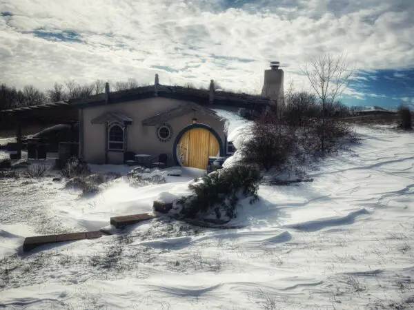 A house with a yellow door in the middle of snow.