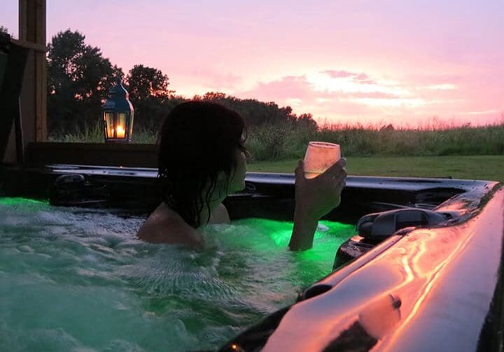 Woman in hot tub with a glass of wine looking out at a beautiful sunset.